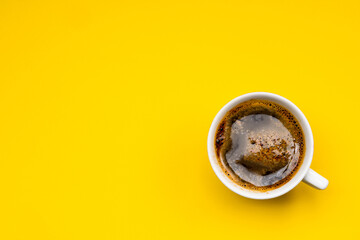 Frothy coffee in a porcelain cup on yellow background