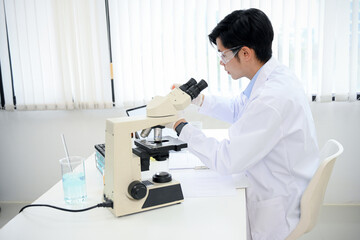 A handsome Asian male scientist examining a virus specimen under a microscope in the lab.