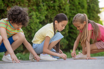 Two girls and boy painting on asphalt