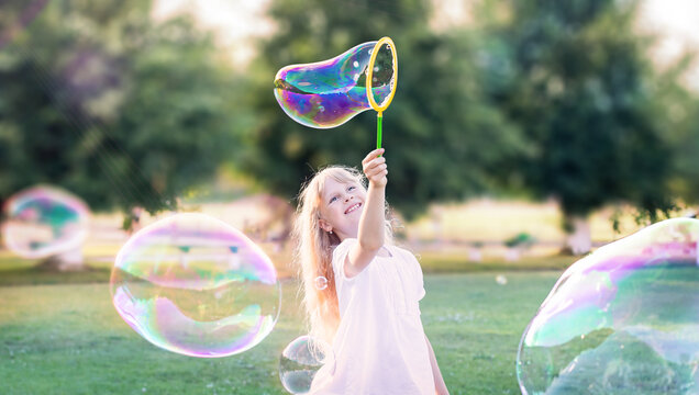 Child girl plays, inflates bubbles in the garden.