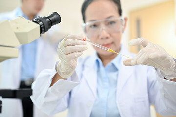 Asian senior female scientist using a dropping a virus sample into a microscope slide
