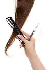 A woman's hand holds a comb, hairdressing scissors near brown hair. The position of readiness for the cutting process. Providing hairdressing services, hair care, haircuts. Isolated on white backgroun