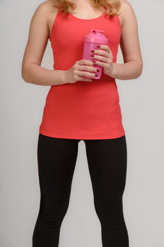 Female fitness model in sportswear posing with water bottle on gray background