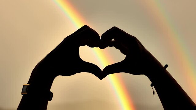 Woman Hand Making Heart Shape Against a Rainbow with Yellow Sky in Switzerland.