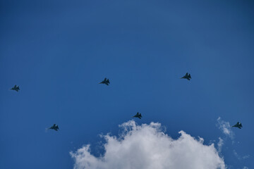 Parade of army air force over the city. Group of military aircraft shows aerobatics in blue sky against background of clouds. Performance of victory.