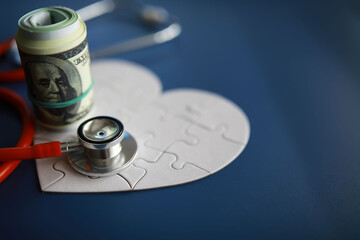 A stethoscope on money and a puzzle heart. Health insurance. Healthcare and medicine. How much is the treatment. Money and medicine. World Heart Day. World Health Day.