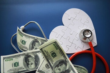 A stethoscope on money and a puzzle heart. Health insurance. Healthcare and medicine. How much is...
