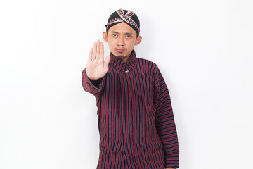 asian man with javanese traditional cloth lurik with open hand doing stop sign with serious expression defense gesture isolated on white background