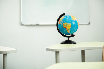 The Globe stands on the desk in the school classroom against the white school board. Planet Earth. Back to school concept. Classroom interior design