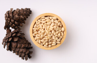 Heap of pine nuts and wood cup and cedar cones on white background
