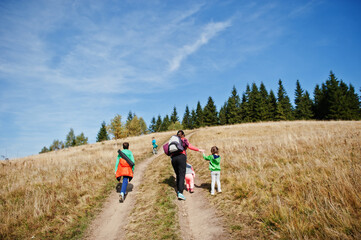 Fototapeta premium Woman is traveling with a childrens. Mom in the mountains. Climb to the top of the mountain with children. With the backpack climbed to the top.