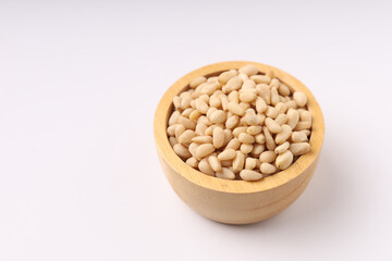 Heap of pine nuts and wood cup and cedar cones on on white background