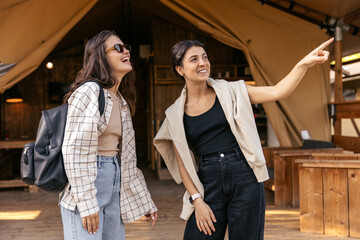 Cheerful young caucasian women are viewing area near glamping site on vacation. Brunettes wear casual clothes in spring. Leisure lifestyle and beauty concept.