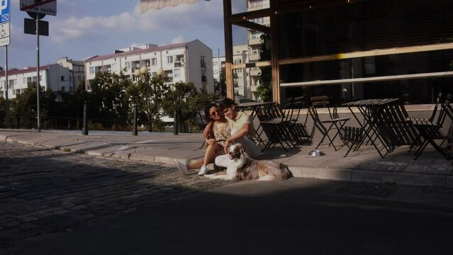 a young latino woman and a young white man sitting outside a cafe with a border collie dog