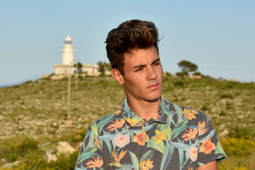 Guy posing on the beach alone, surrounded by Mediterranean vegetation near a lighthouse