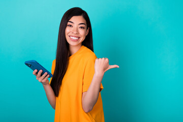 Photo of nice young lady indicate empty space hold telephone wear orange t-shirt isolated on turquoise color background