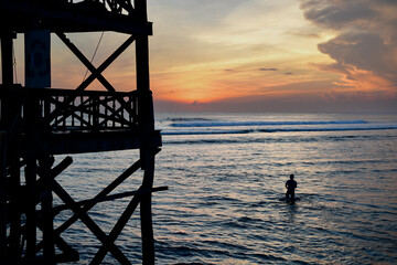 Silhouette of surfer on the pier at sunrise with colorful skies and crystal clear silver waters