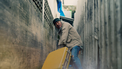 A homeless Asian man is dragging a large suitcase in a narrow alley. to find jobs and food from people who will donate An elderly man with no work, no home, and on the roadside.