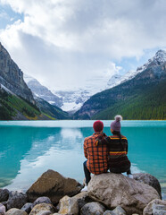 Lake Louise Banff national park is a lake in the Canadian Rocky Mountains. A young couple of men and women sitting on a rock by the lake during a cold day in Autumn in Canada