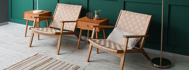 Stylish wicker armchairs with wooden tables near green wall in room