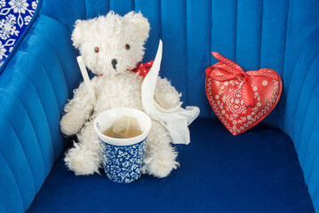 sick teddy bear with fever thermometer, hot tea, handkerchiefs and a red heart on blue velvet...