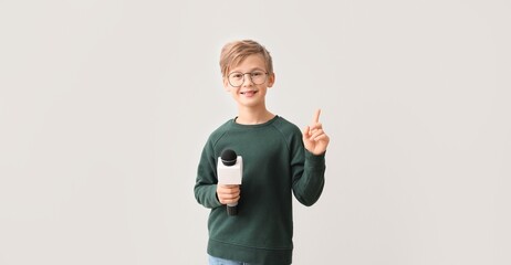 Little journalist with microphone on light background
