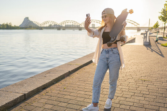 Hipster woman with skateboard. Portrait of urban young girl taking selfie photo.