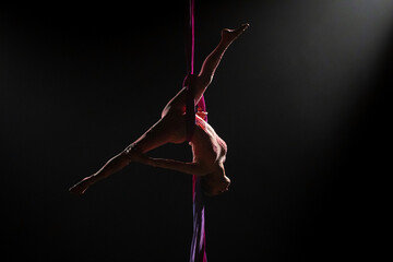 Female circus gymnast hanging upside down on aerial silk and demonstrates stretching. Woman...