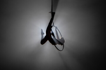 Silhouette of young woman gymnast performs acrobatic stunts on an air hoop under the dome of a...