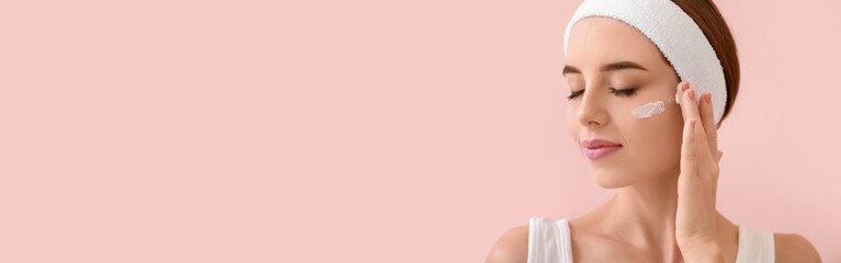 Pretty young woman applying facial cream against pink background with space for text