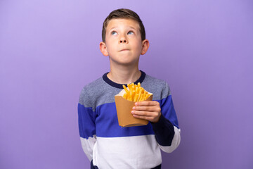 Little boy holding fried chips isolated on purple background and looking up