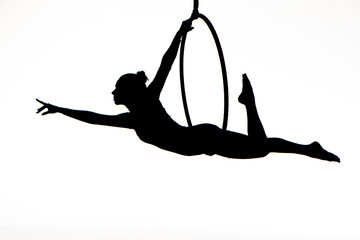 Black silhouette of a young woman posing on an air ring on an isolated white studio background. Female aerial acrobat performs tricks and balances on aerial hoop. Circus acrobatic show. Equilibrist. © kinomaster