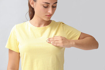 Young woman suffering from breast pain on grey background