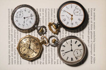 A set of antique gold and silver American and Swiss pocket watches with markings, lying on pages of an open book. Round old clock with white dials, hands and numbers. Presentation of vintage clocks.