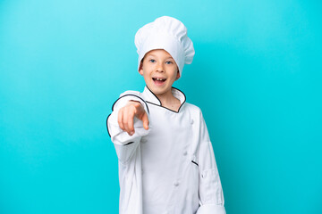 Little chef boy isolated on blue background surprised and pointing front