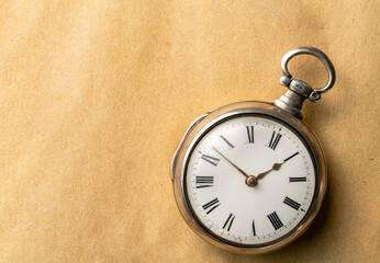 Silver vintage pocket watch with hands and numbers on a round dial. Old retro clock on a beige...