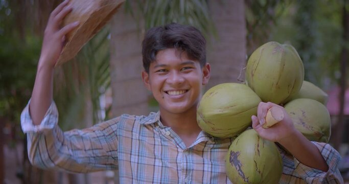 Slow motion happy smiling young Asian farmer take off the hat and carry coconut bunch whose fragrant water and soft flesh are perfect to sell as a beverage or called coconut with a flagrant juice.