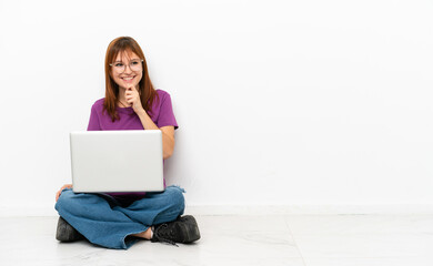 redhead girl with a laptop sitting on the floor looking to the side and smiling