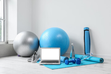 Modern laptop and sports equipment on floor near white wall