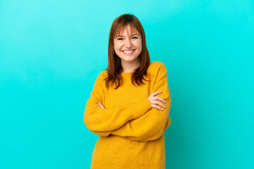 Redhead girl isolated on blue background keeping the arms crossed in frontal position