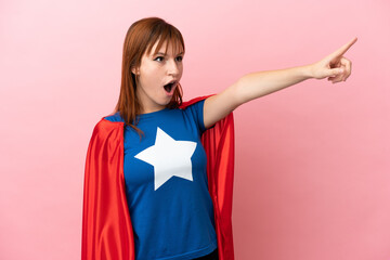 Super Hero redhead girl isolated on pink background pointing away © luismolinero