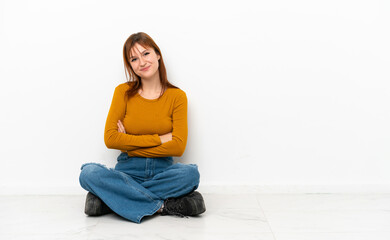 Fototapeta na wymiar Redhead girl sitting on the floor isolated on white background with arms crossed and looking forward
