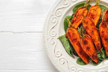 Plate of tasty baked carrots on light wooden background