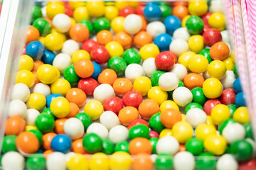 Fototapeta na wymiar Closeup of multi color candy balls in transparent box in candy shop. Low sugar fruit gummies, hues come from fruit and veggie juices. Smart healthy living. Horizontal plane