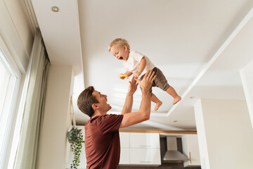 Young dad throwing excited laughing baby boy up in air and catching, amusing kid and having fun...