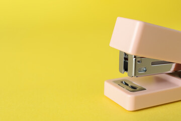 Pink stapler on yellow background, closeup