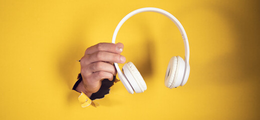 hand holding headphones on yellow background
