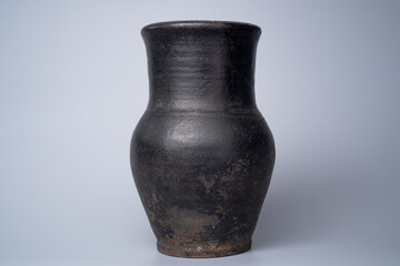Black shabby jug, handmade jar from clay on gray background in the studio. Earthenware for drink...