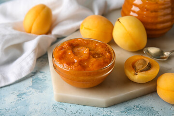 Board with bowl of tasty apricot jam and fruits on color background