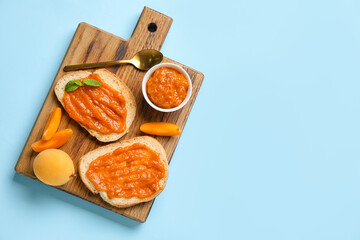 Wooden board of tasty sandwiches with apricot jam on color background